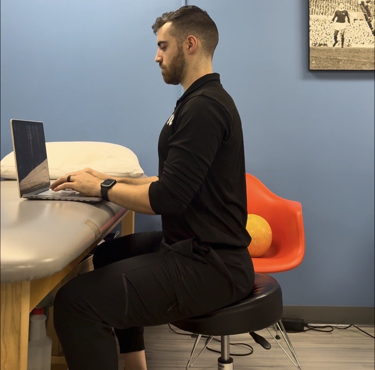 Dr. Brad sitting upright at a laptop on a stool
